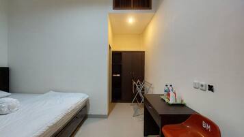 Une chambre à coucher comprenant un lit, un bureau avec une chaise, une armoire et une petite table sur laquelle sont posés divers objets.