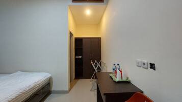 Una habitación pequeña y bien iluminada, con una cama, un escritorio con silla y un armario.