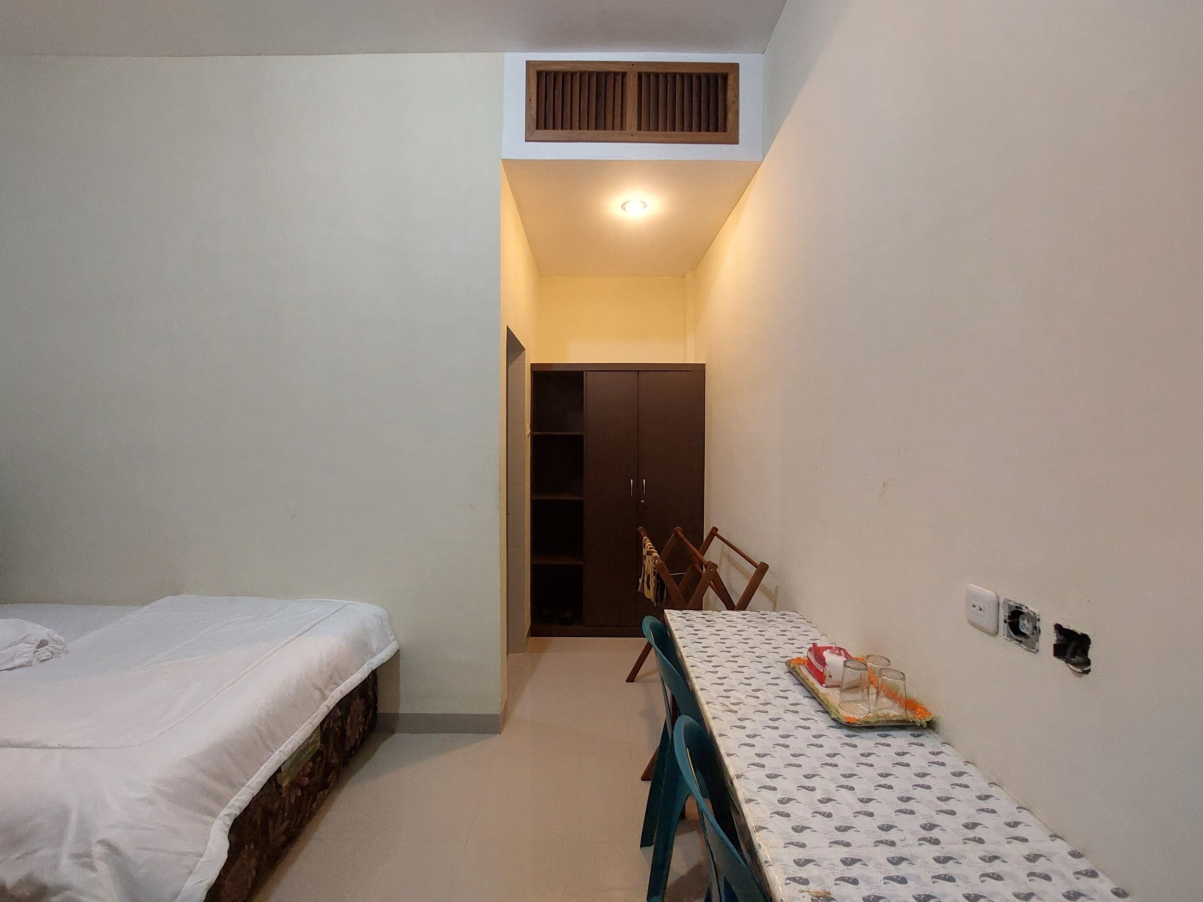A small, well-lit room with a bed, a table with a tray of items, and a door leading to another room.