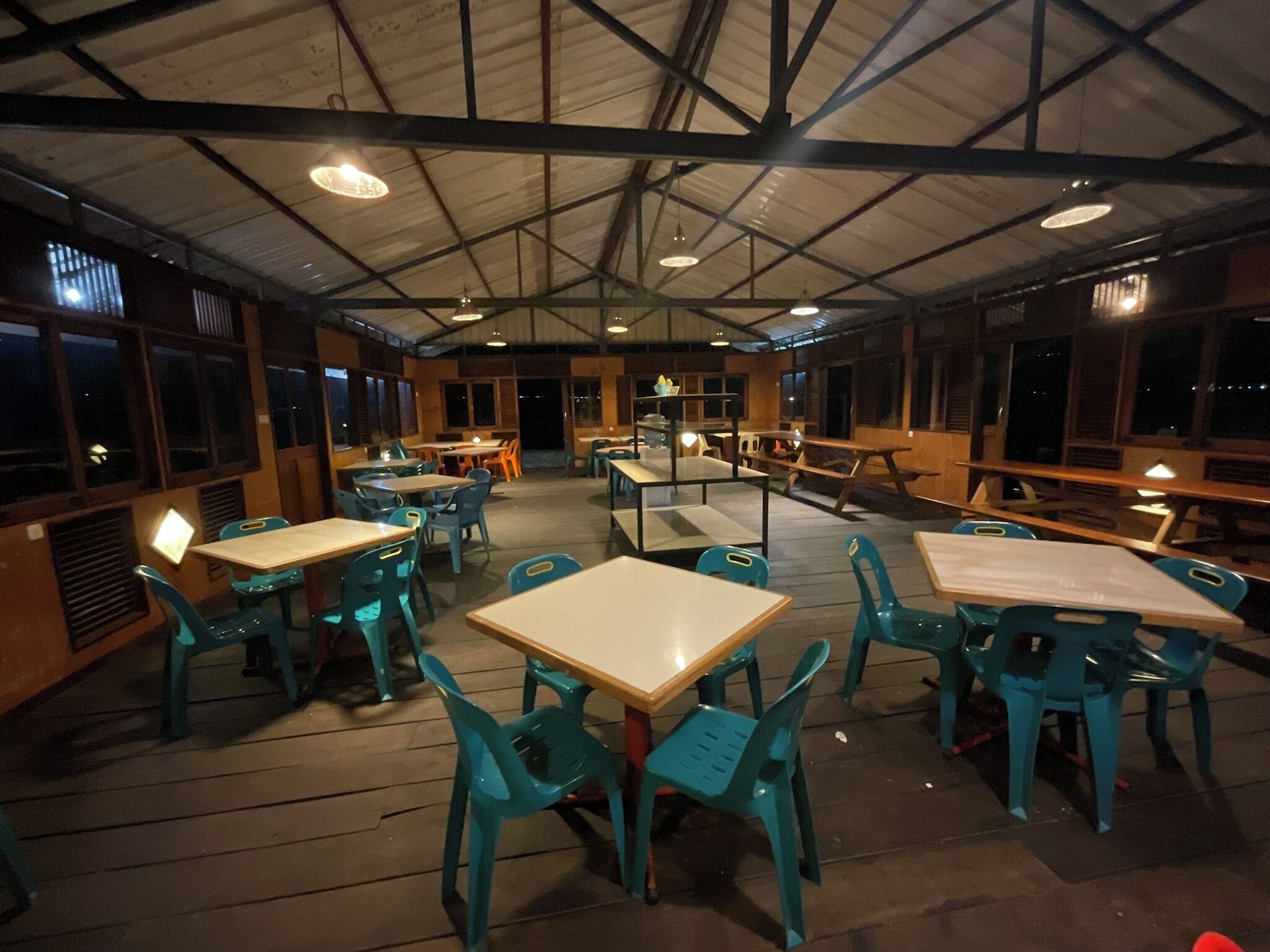 Un comedor interior con mesas y sillas, suelo de madera y un techo alto con vigas a la vista.