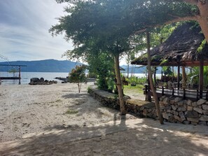 A beach with a wooden gazebo, a swing set, and a stone wall. - Gondang Sivali Hotel (Samosir)