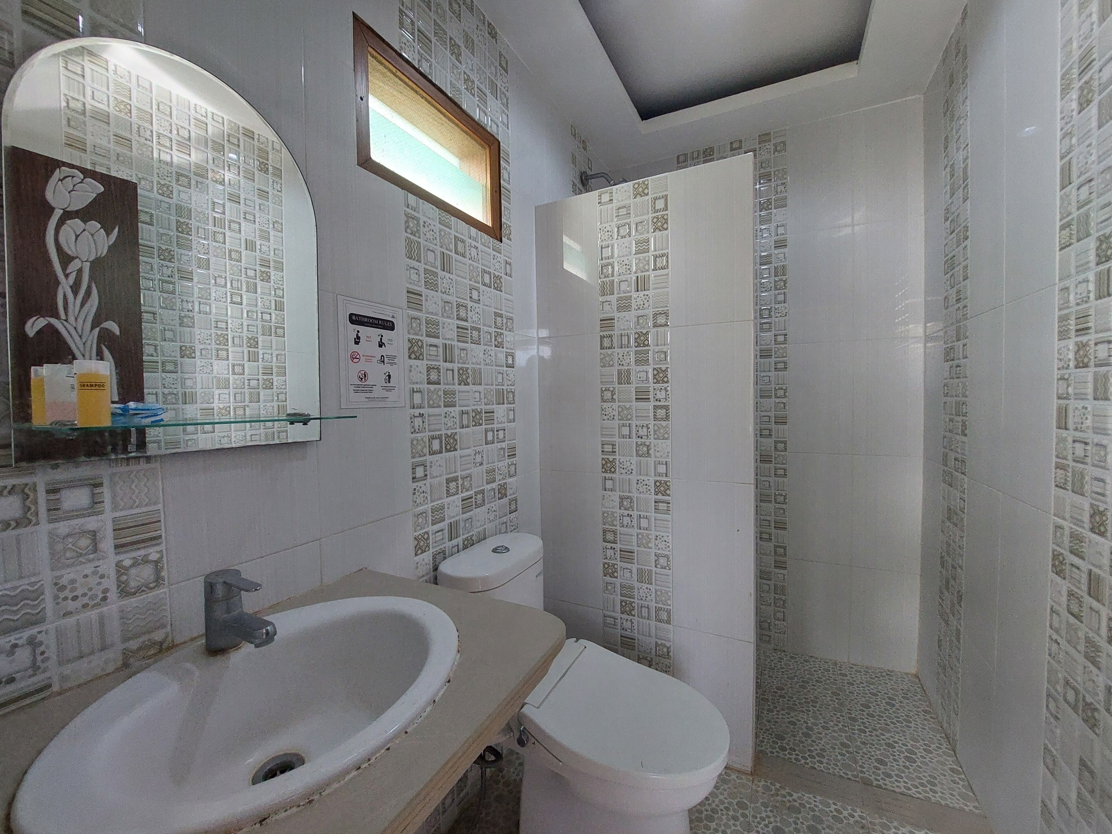 Casa de banho com lavatório, sanita e chuveiro. As paredes estão revestidas com diversos padrões.