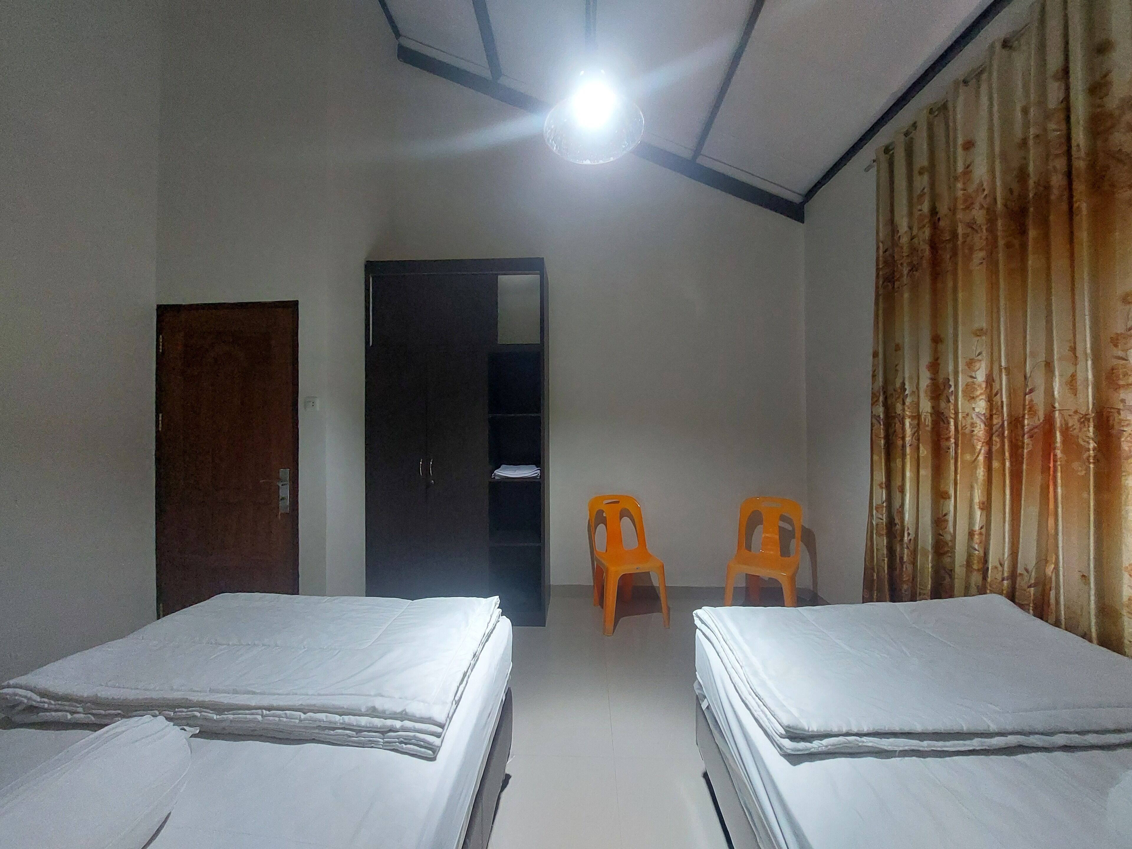 Quarto com duas camas, um guarda-roupa, uma porta e duas cadeiras laranja.