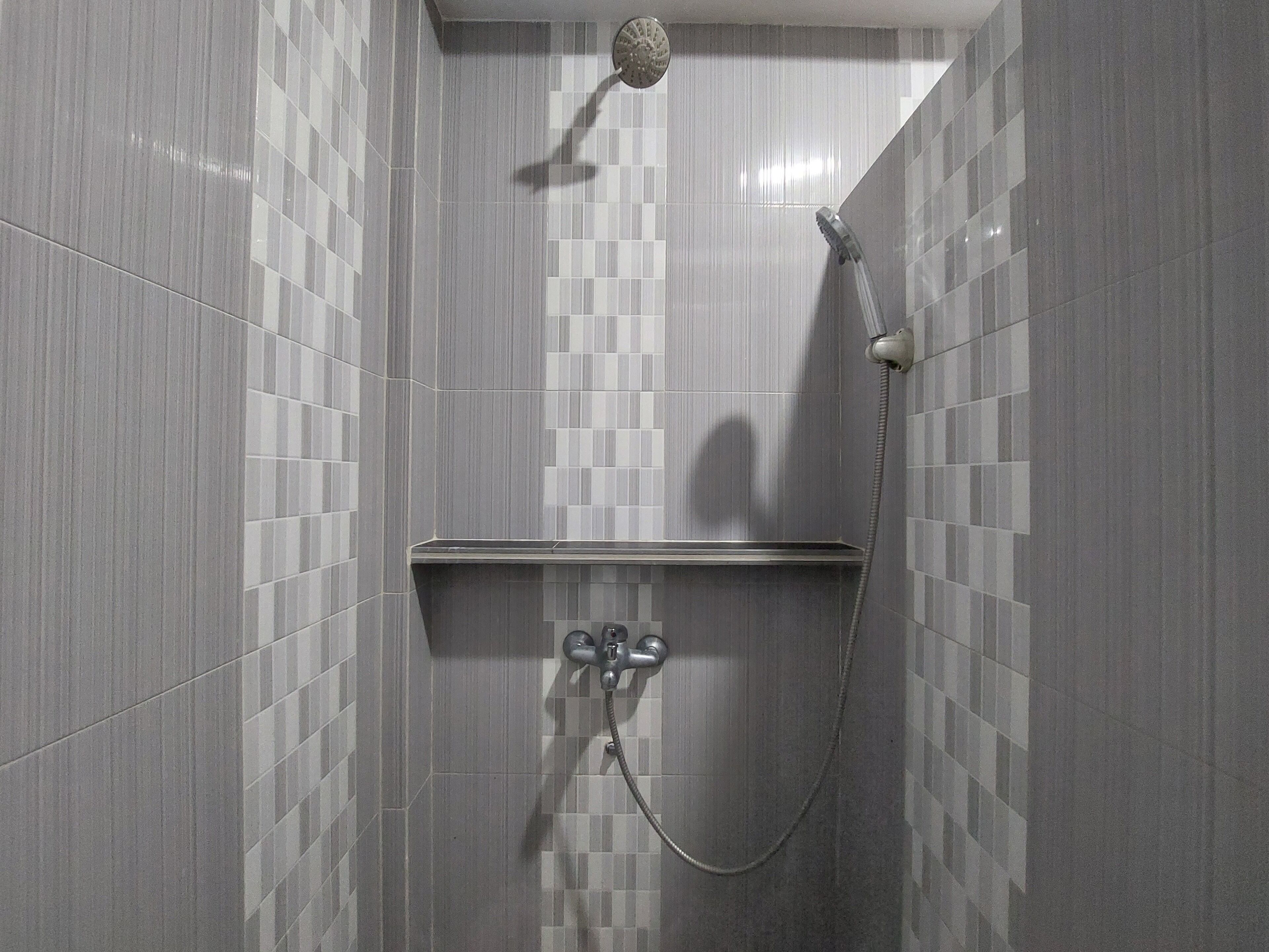 Área de duche com chuveiro manual e torneira fixa na parede.