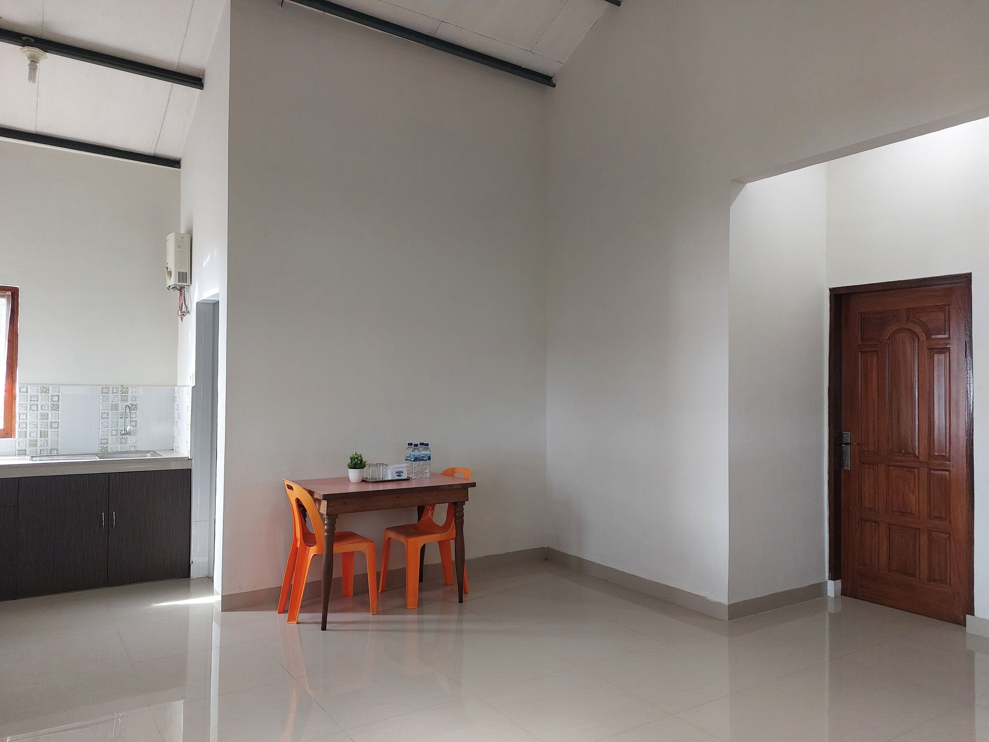 A room with a kitchen area, a dining table with chairs, and a wooden door.