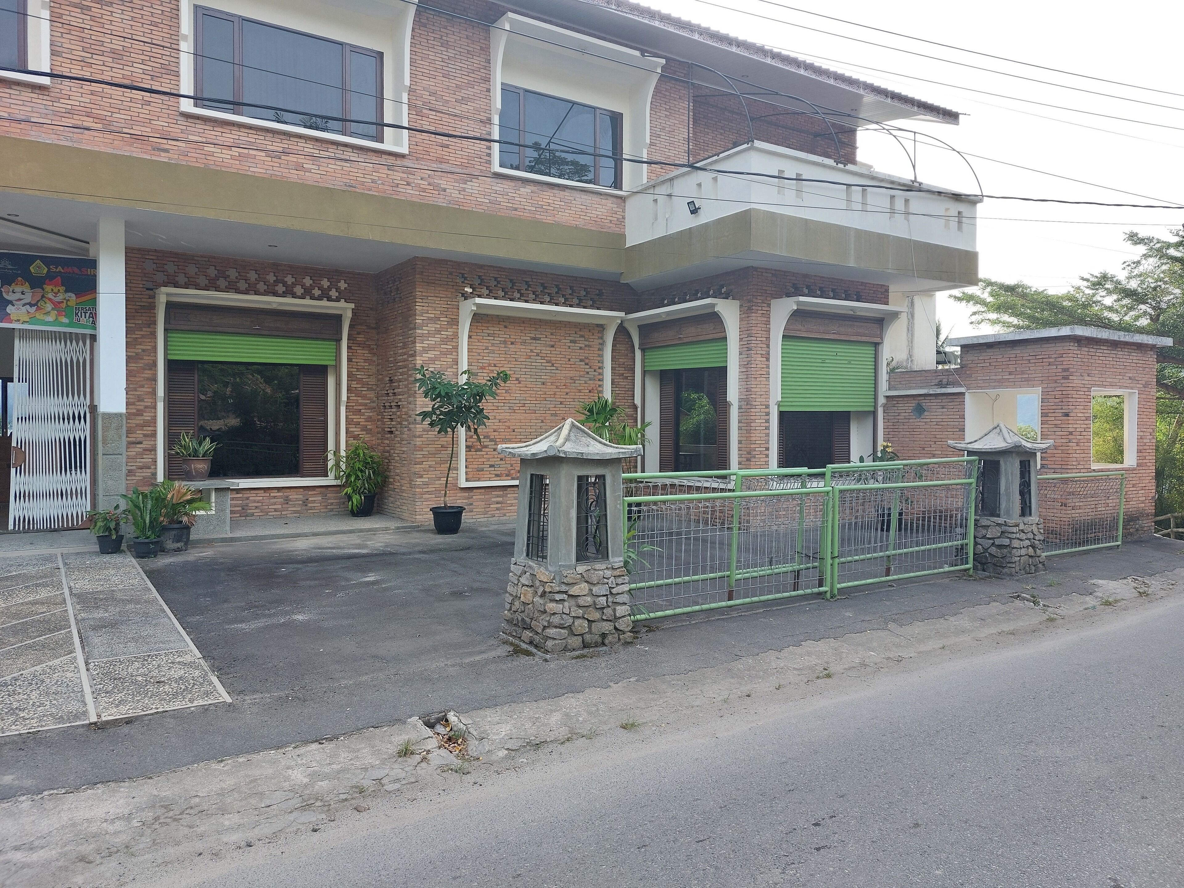 A two-story brick house with green shutters, a gated entrance, and potted plants.