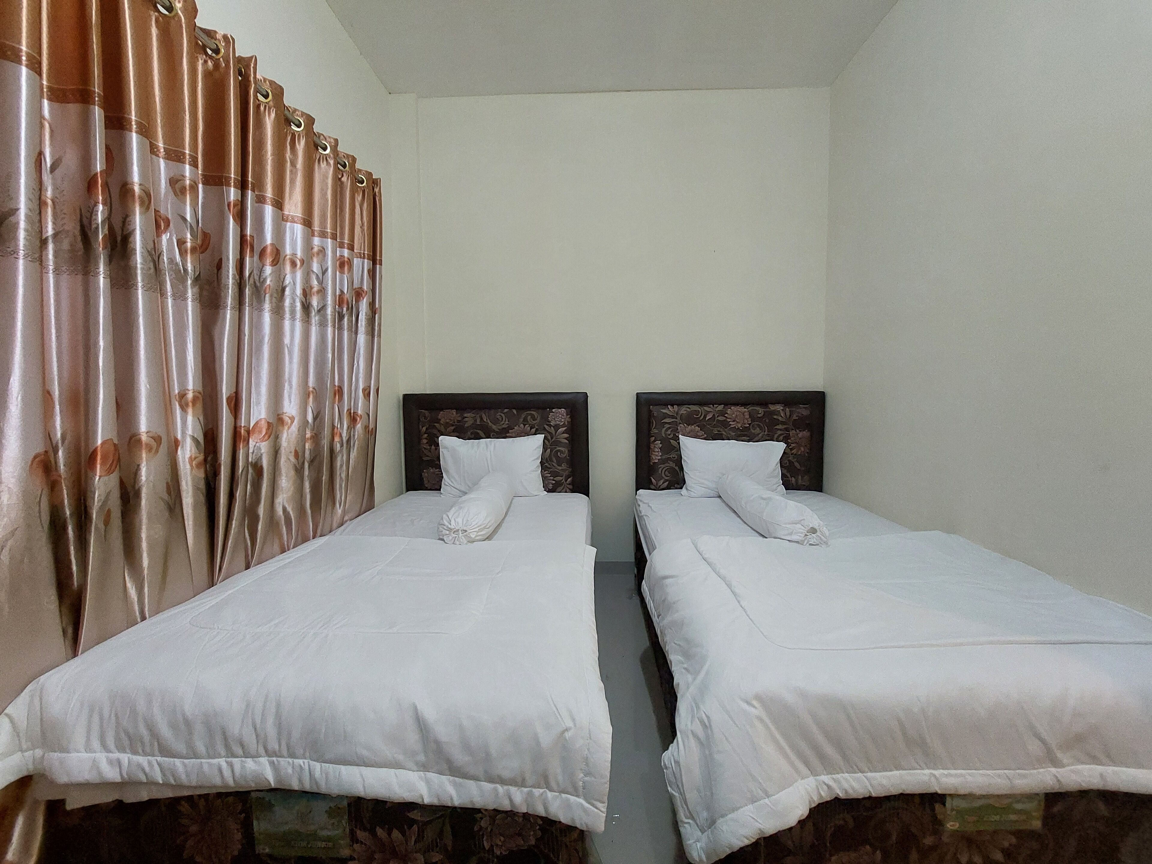 A room with two single beds, each with a wooden headboard and white bedding.