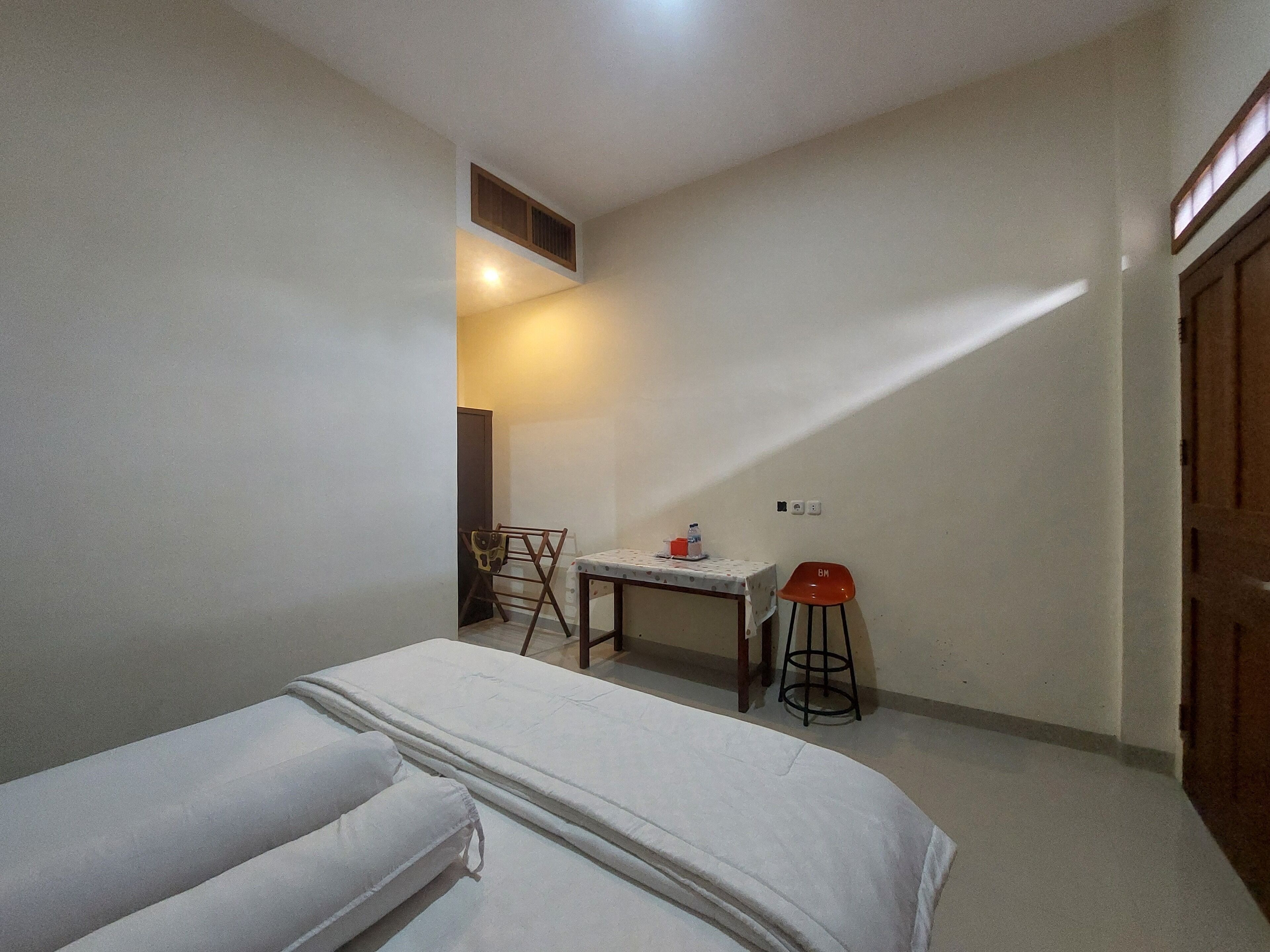 Un dormitorio con cama, una mesita, una silla y una ventana.
