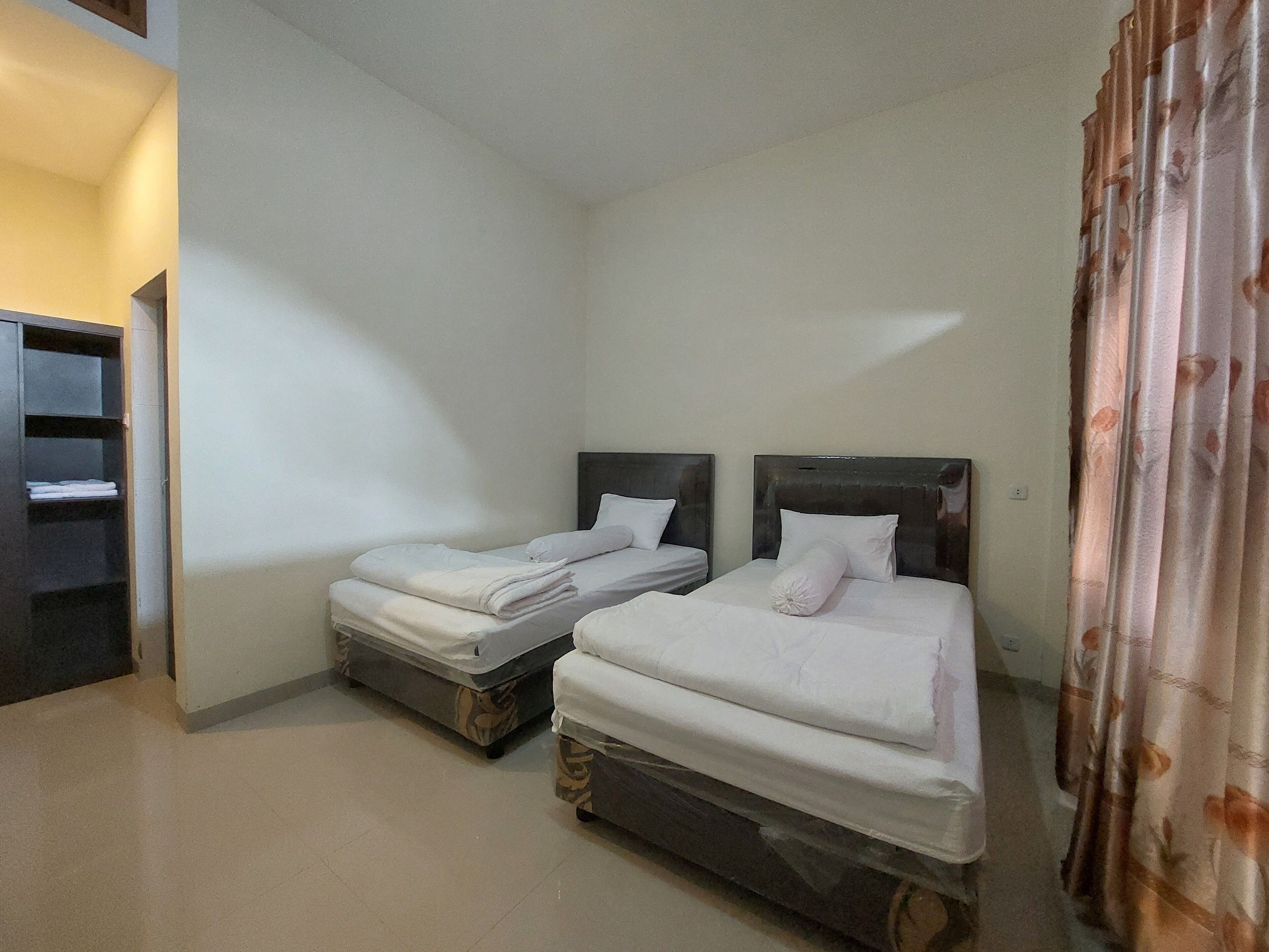 Una habitación con dos camas, cada una con cabecera y almohadas, un armario y una cortina.