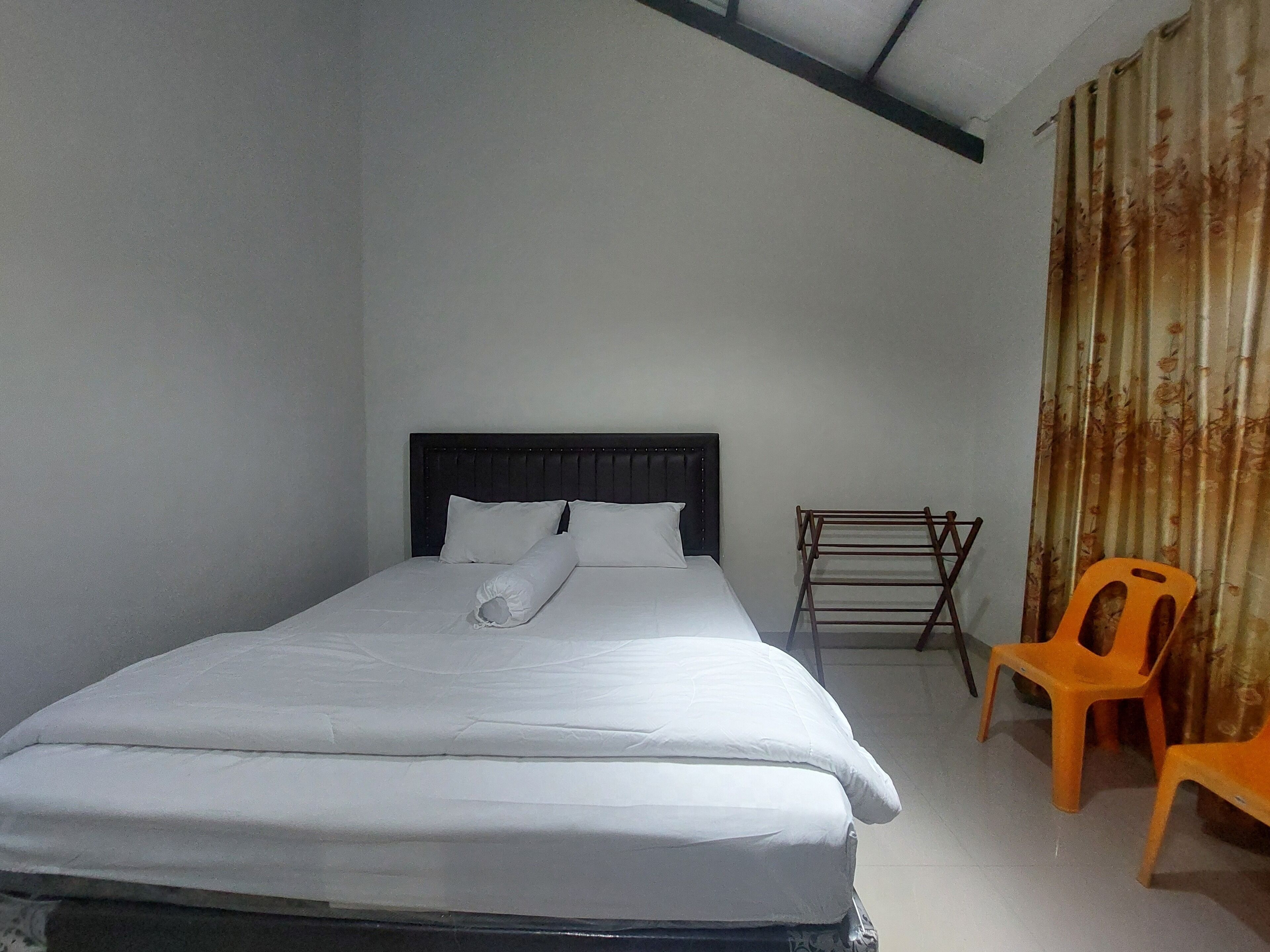 A neatly made bed with white linens, a dark headboard, and a wooden drying rack to the right.