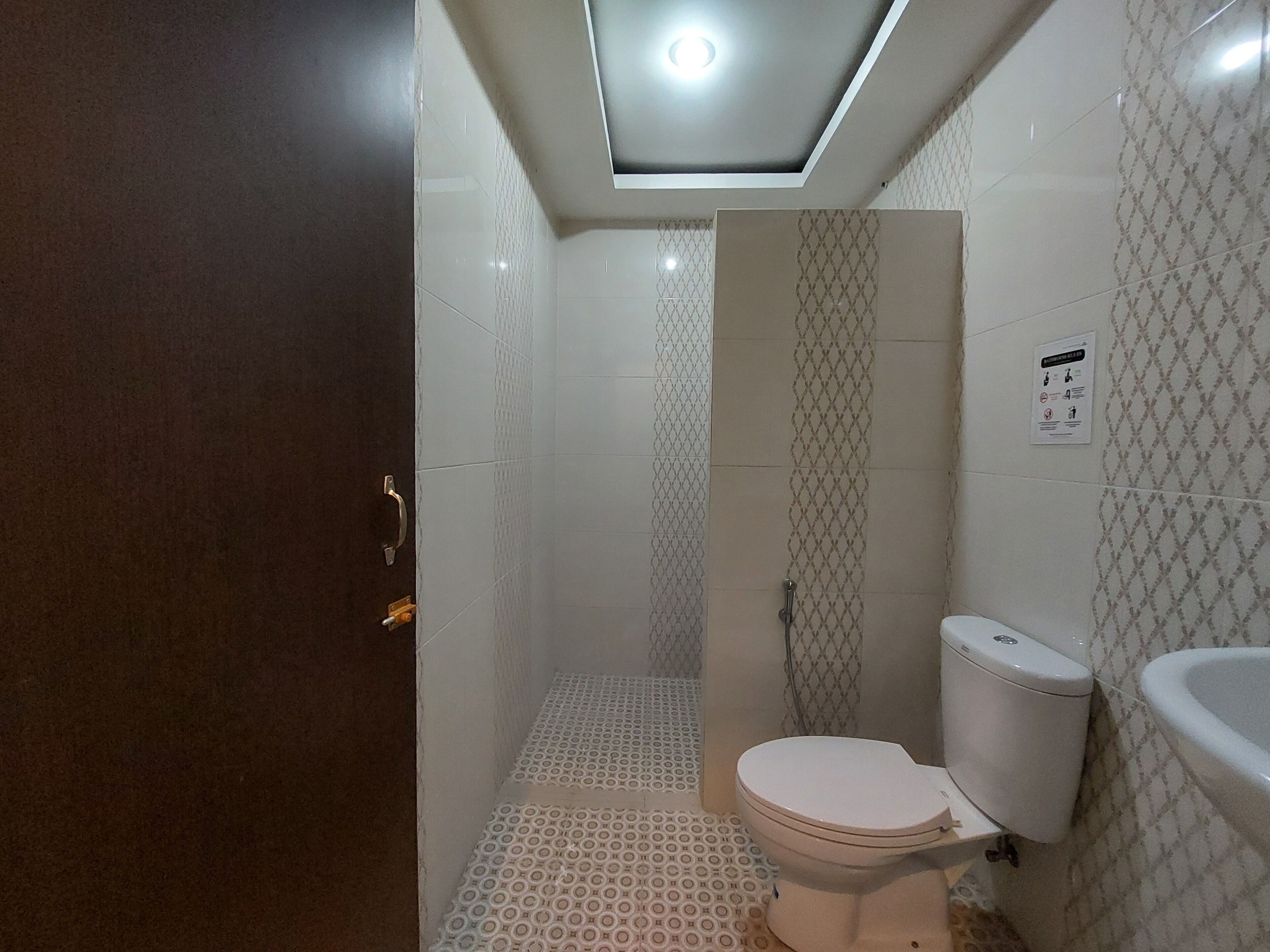 Un baño pequeño y funcional con inodoro, lavamanos y ducha. Las paredes están cubiertas con un patrón geométrico de azulejos, y hay un accesorio de iluminación en el techo.