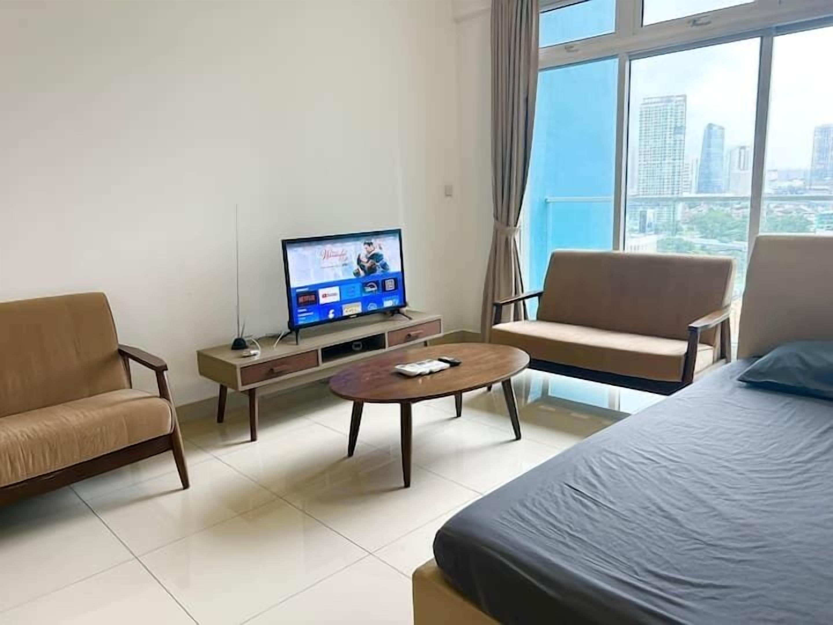 A hotel room with a bed, two armchairs, a coffee table, and a TV on a wooden stand.