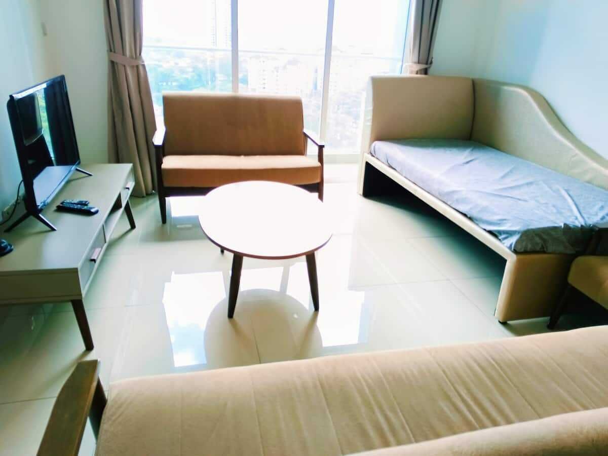 A modern hotel room with a sofa, a small round table, a TV, and a bed.