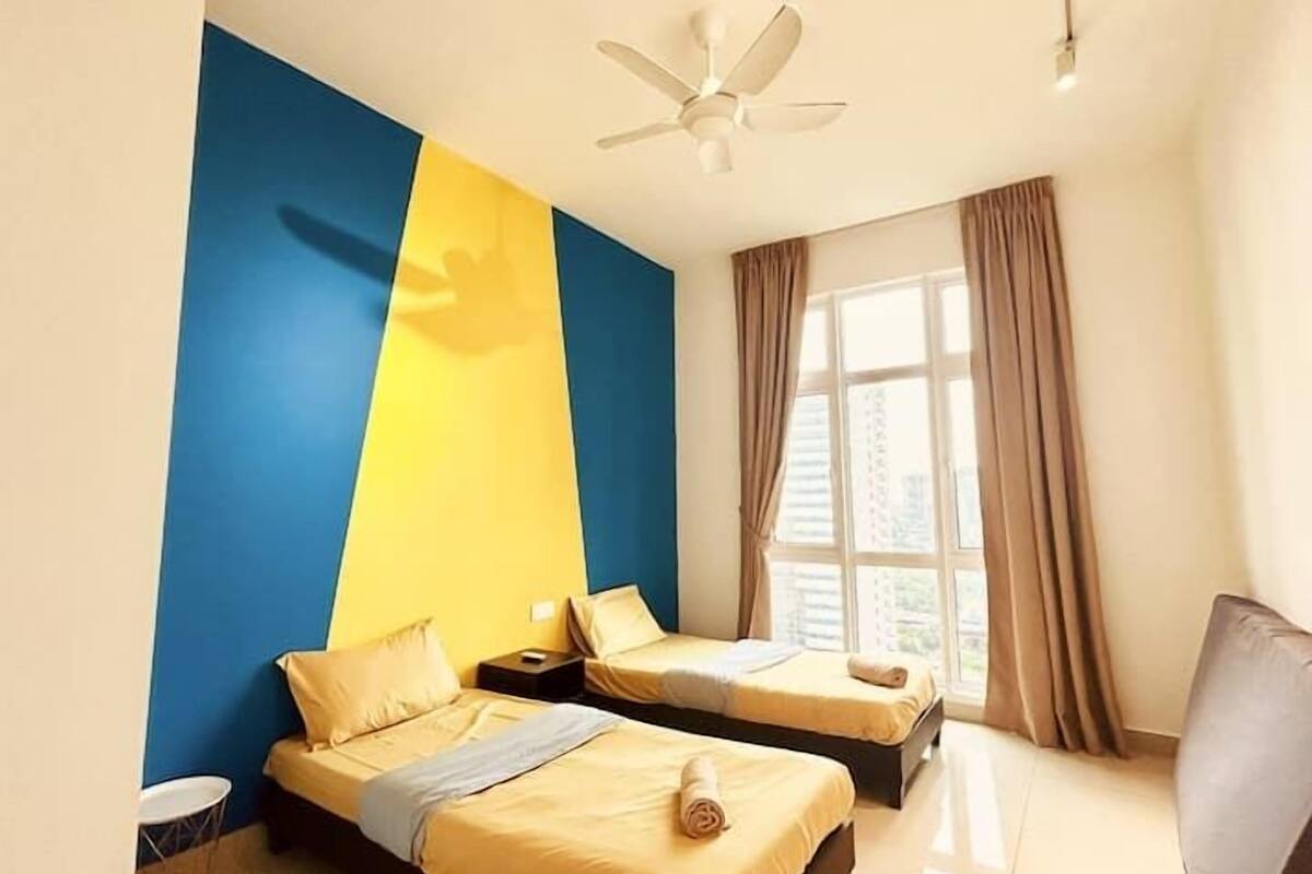 A hotel room with two beds, a ceiling fan, a window with curtains, and a small round table.