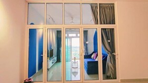 A room with a large sliding glass door leading to a balcony. The room has a television, a small table with a vase, and a sofa with cushions. - Twin Galaxy (Johor Bahru)