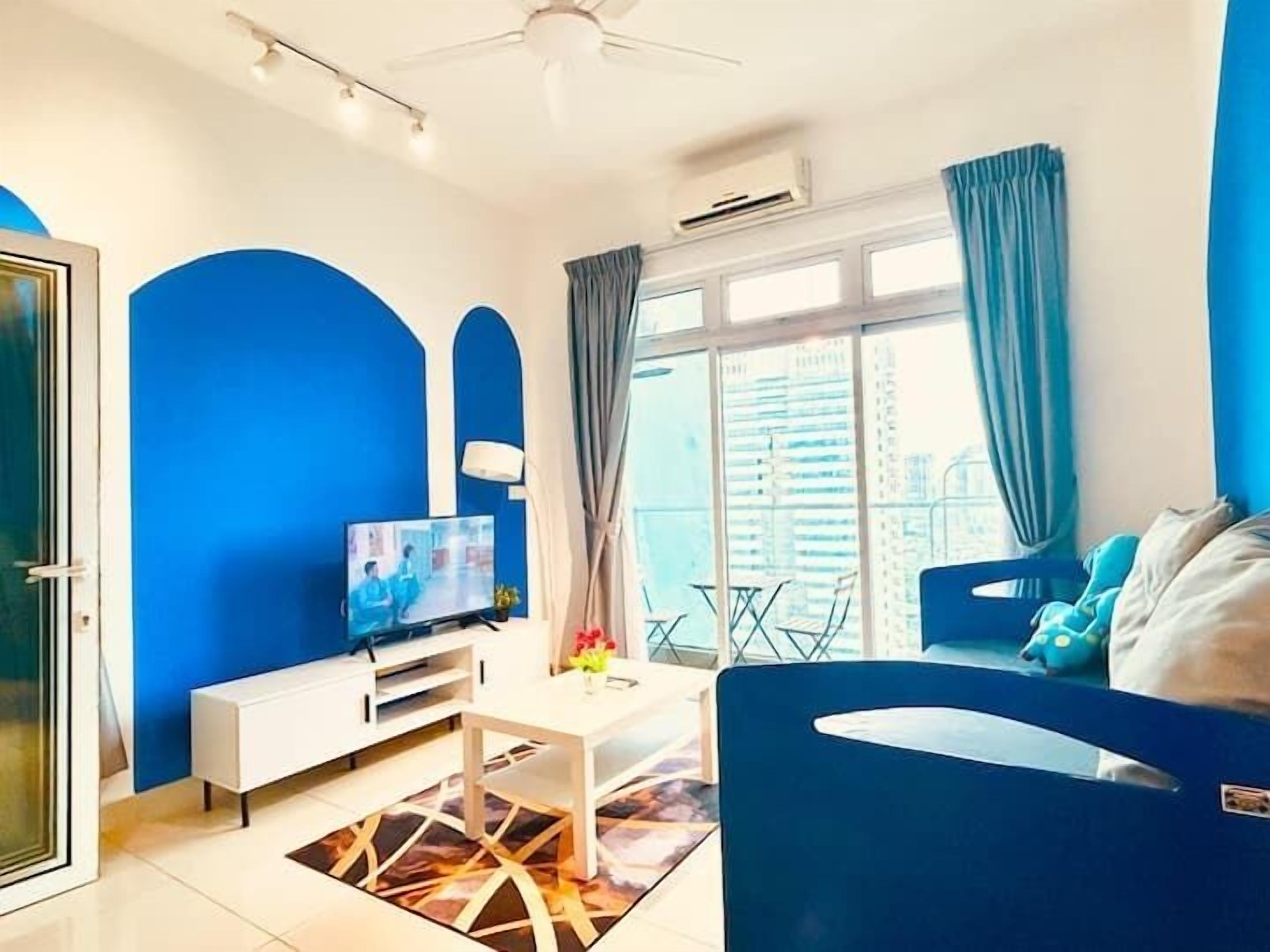 A modern living room with a TV, white furniture, and a view of the city through large windows.