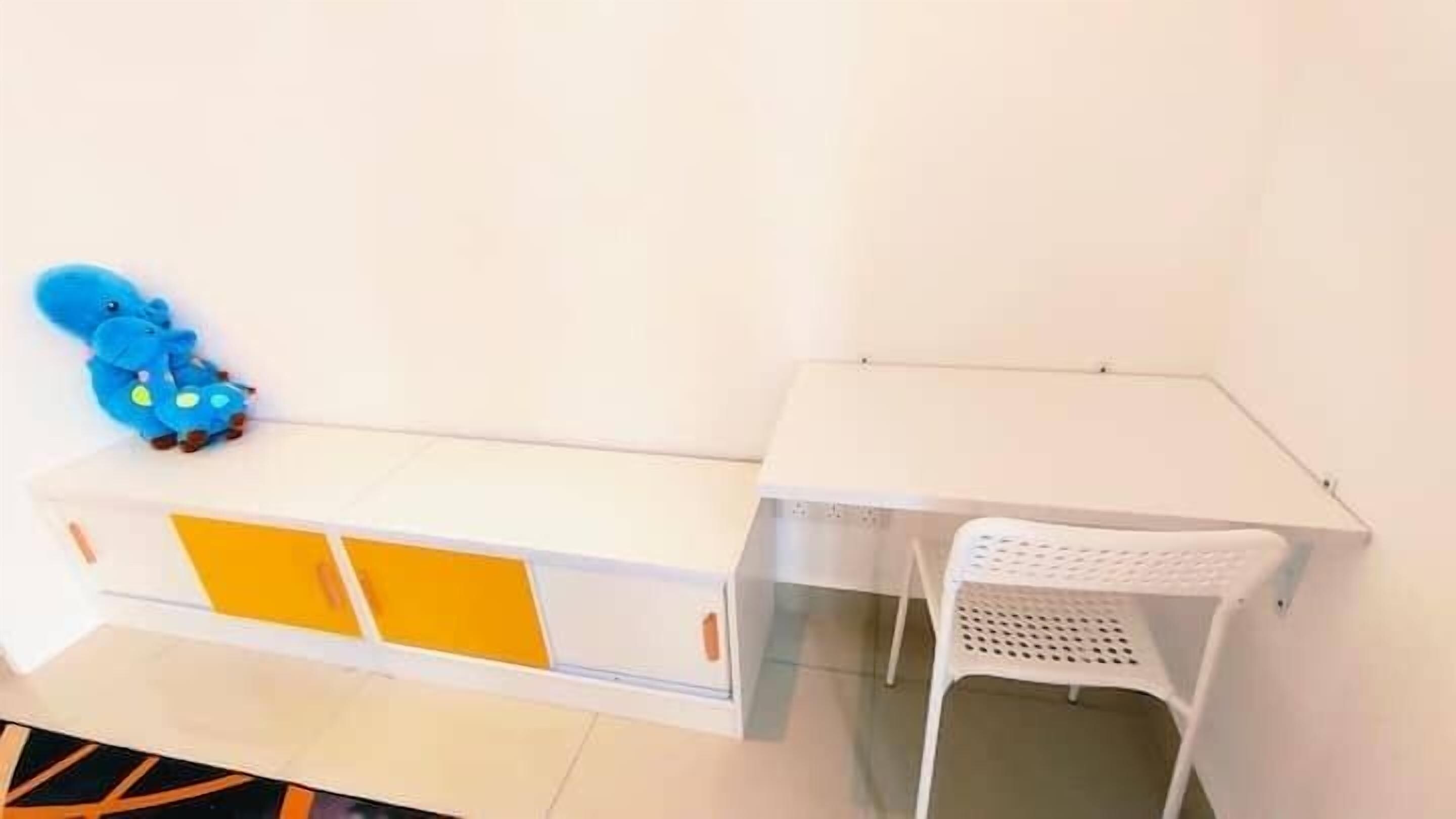 A white room with a white desk and a white chair. There is a blue toy elephant on the desk.