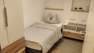 A small, neatly arranged bedroom with a bed, bedside table, and a window.