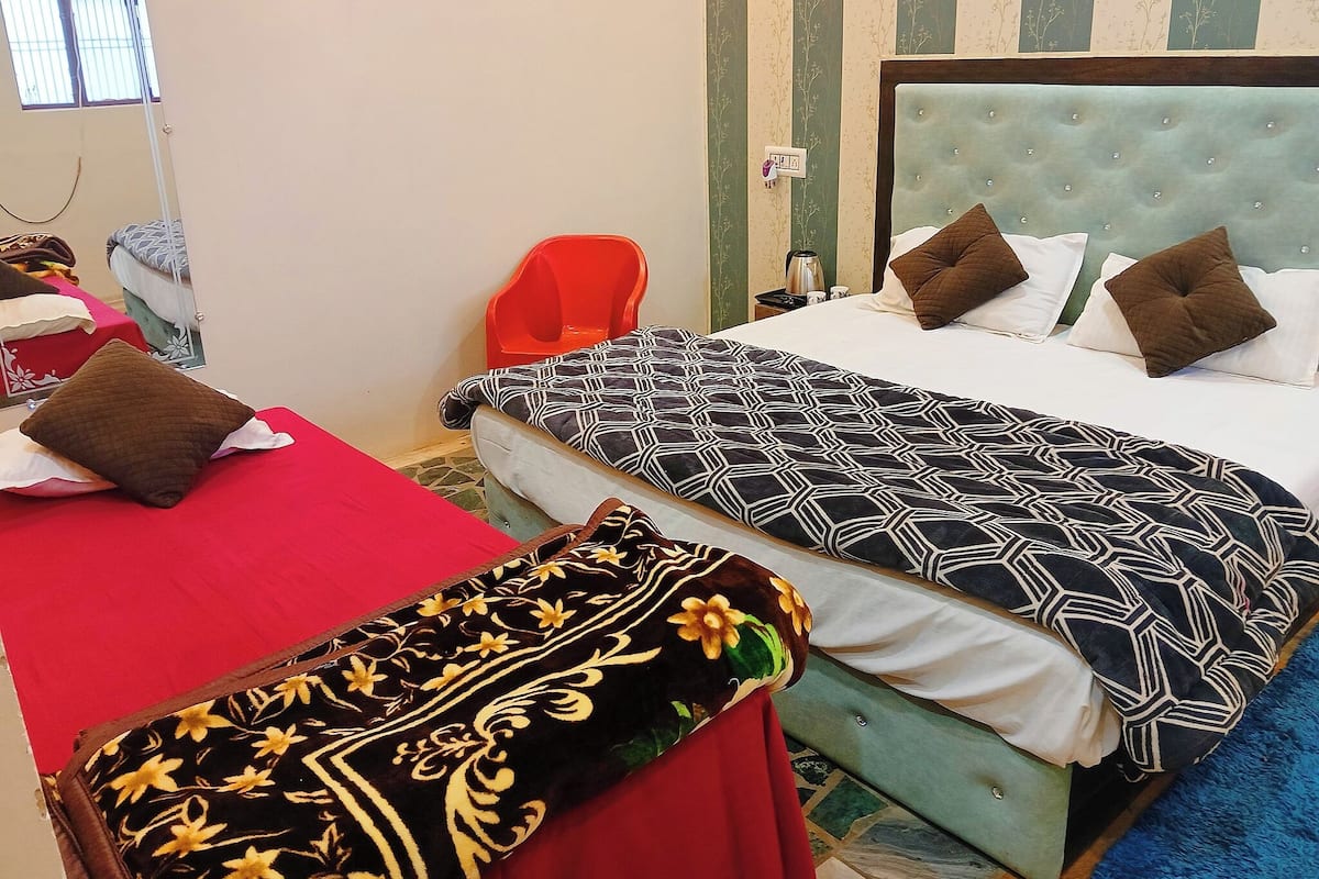 Habitación de hotel con dos camas, una colcha roja, una manta estampada y una colcha azul.