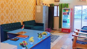 A reception area with a blue counter, green upholstered seating, a refrigerator, a Coca-Cola refrigerator, and a flag on the counter.