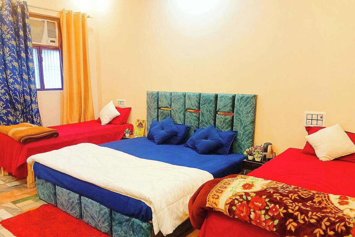 Habitación de hotel con una cama grande, dos camas más pequeñas, un tapete rojo y una ventana con cortinas.