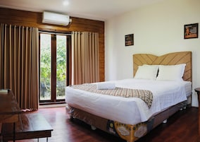 Habitación de hotel con una cama grande, paneles de madera en las paredes, una ventana con cortinas y un aire acondicionado de pared.