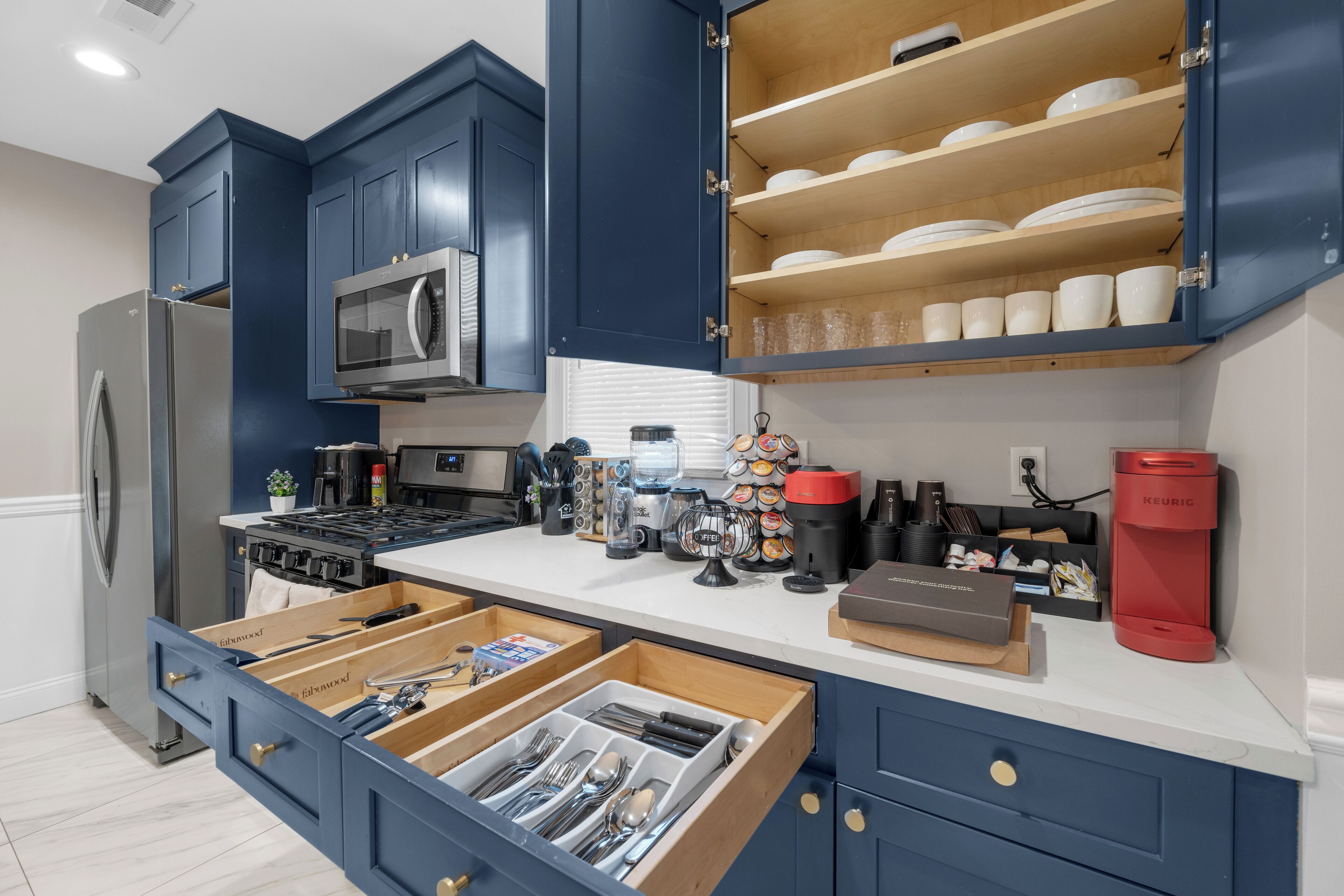 A modern kitchen with dark blue cabinets, a stainless steel refrigerator, a microwave, and a coffee maker.