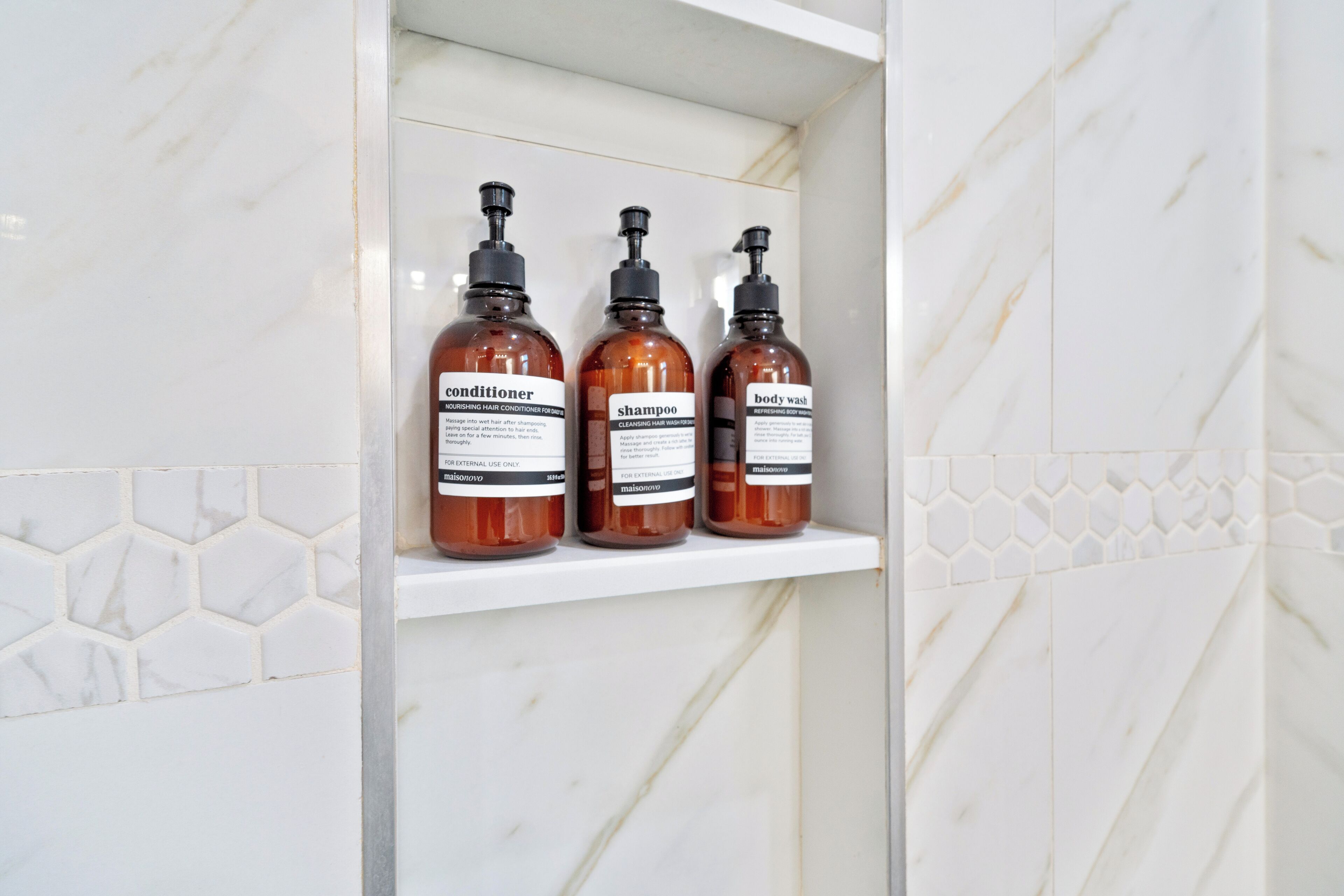 A bathroom shelf with three toiletry bottles labeled conditioner, shampoo, and body wash.