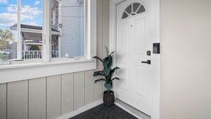 Una puerta blanca con una pequeña ventana, una planta en maceta y un timbre.