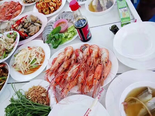 Une table où l’on trouve divers plats, notamment des crevettes, des légumes et des sauces.