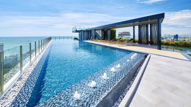A modern infinity pool with a clear view of the ocean, a covered outdoor area with lounge chairs, and a cityscape in the background. - Best Pool With 360 View of Pattaya & Best Location (Pattaya)