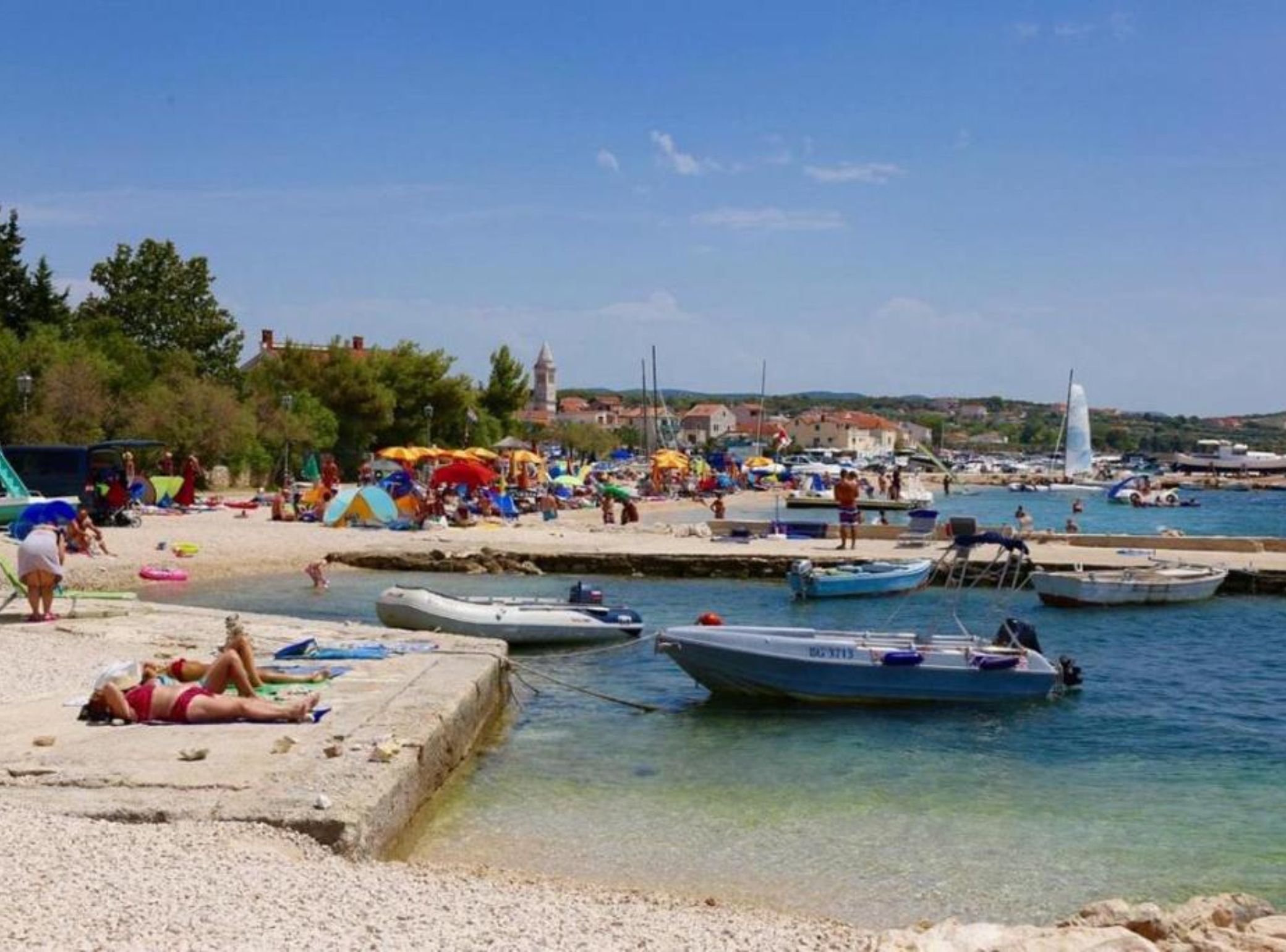 A beach with boats docked, people sunbathing, and a clear sky.