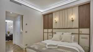 A modern bedroom with a large bed, a headboard with built-in lighting, and a visible door leading to another room. - Superb AC Apartment Roosevelt Saint Honore (Paris)
