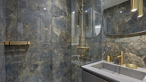 A modern bathroom with marble walls, a glass-enclosed shower, and a vanity with gold fixtures. - Superb AC Apartment Roosevelt Saint Honore (Paris)