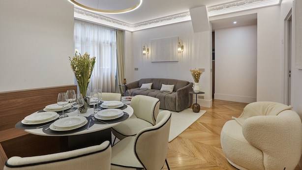 A modern dining area with a round table set for four, a sofa, and a decorative vase with flowers. - Superb AC Apartment Roosevelt Saint Honore (Paris)