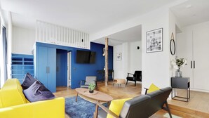 En moderne stue med en gul sofa, en sort sofa, et træbord og en blå måtte.