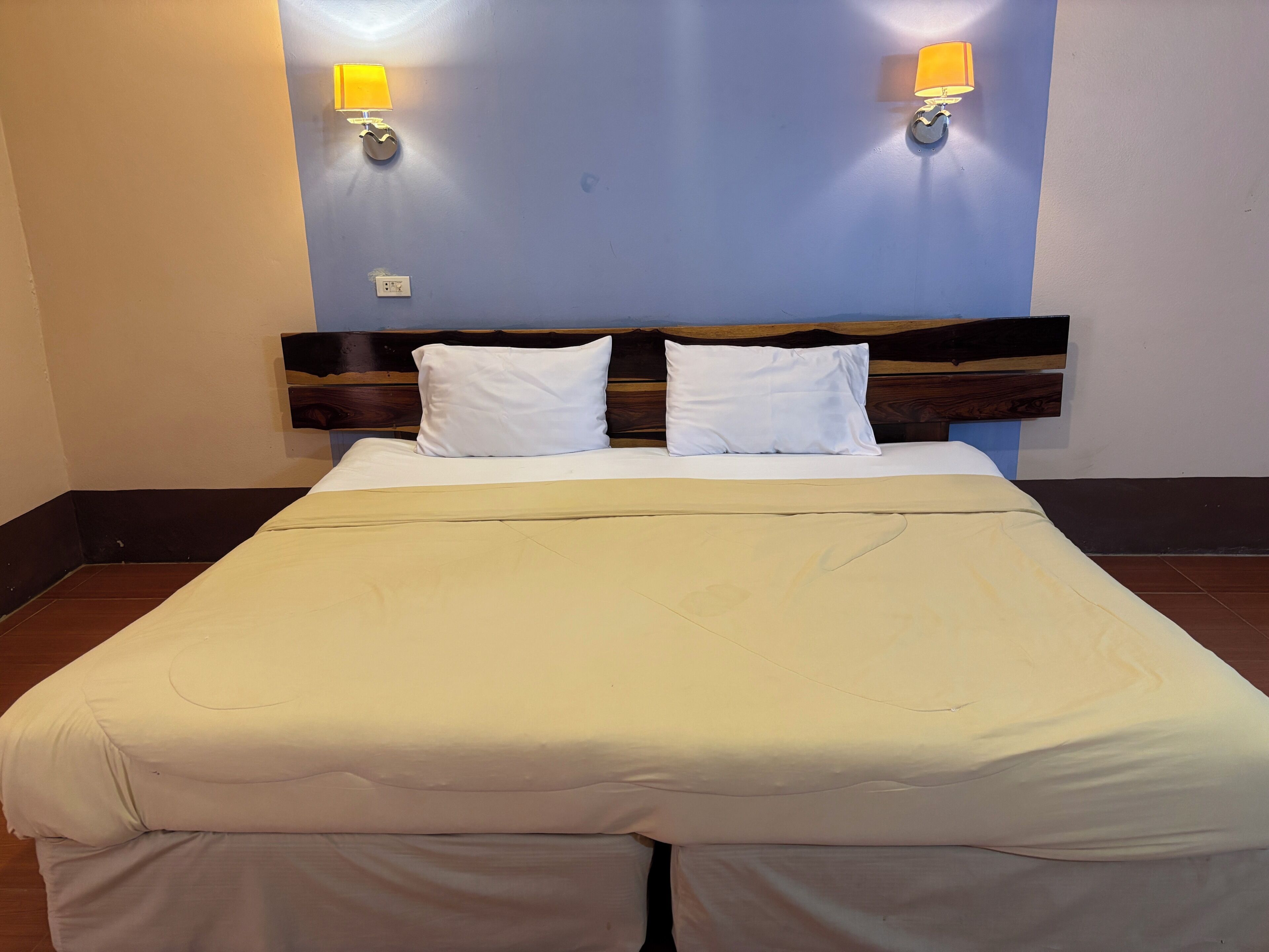 A neatly made bed with white linens, a wooden headboard, and two wall-mounted lamps.
