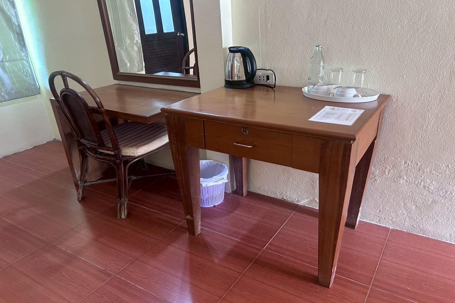 A wooden desk with a chair, a kettle, and a tray with glasses and a bottle.
