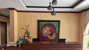 Balcão de recepção com uma obra de arte emoldurada acima, um vaso de flores e um banco de madeira à esquerda.