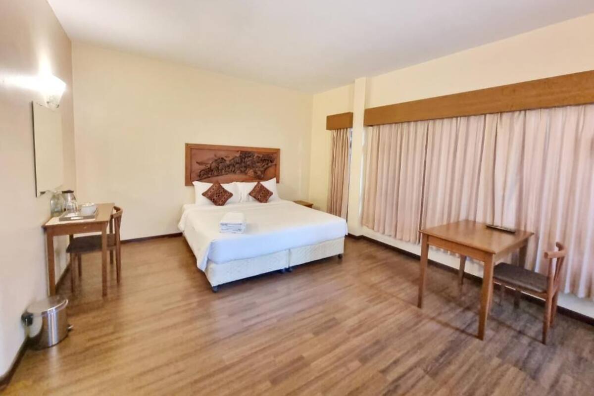 A hotel room with a bed, a wooden table, a chair, a desk, and a lamp.