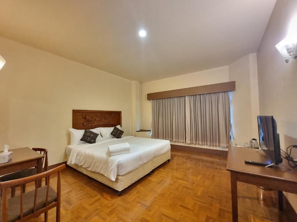 A hotel room with a bed, a desk, a chair, a TV, and a window with curtains.