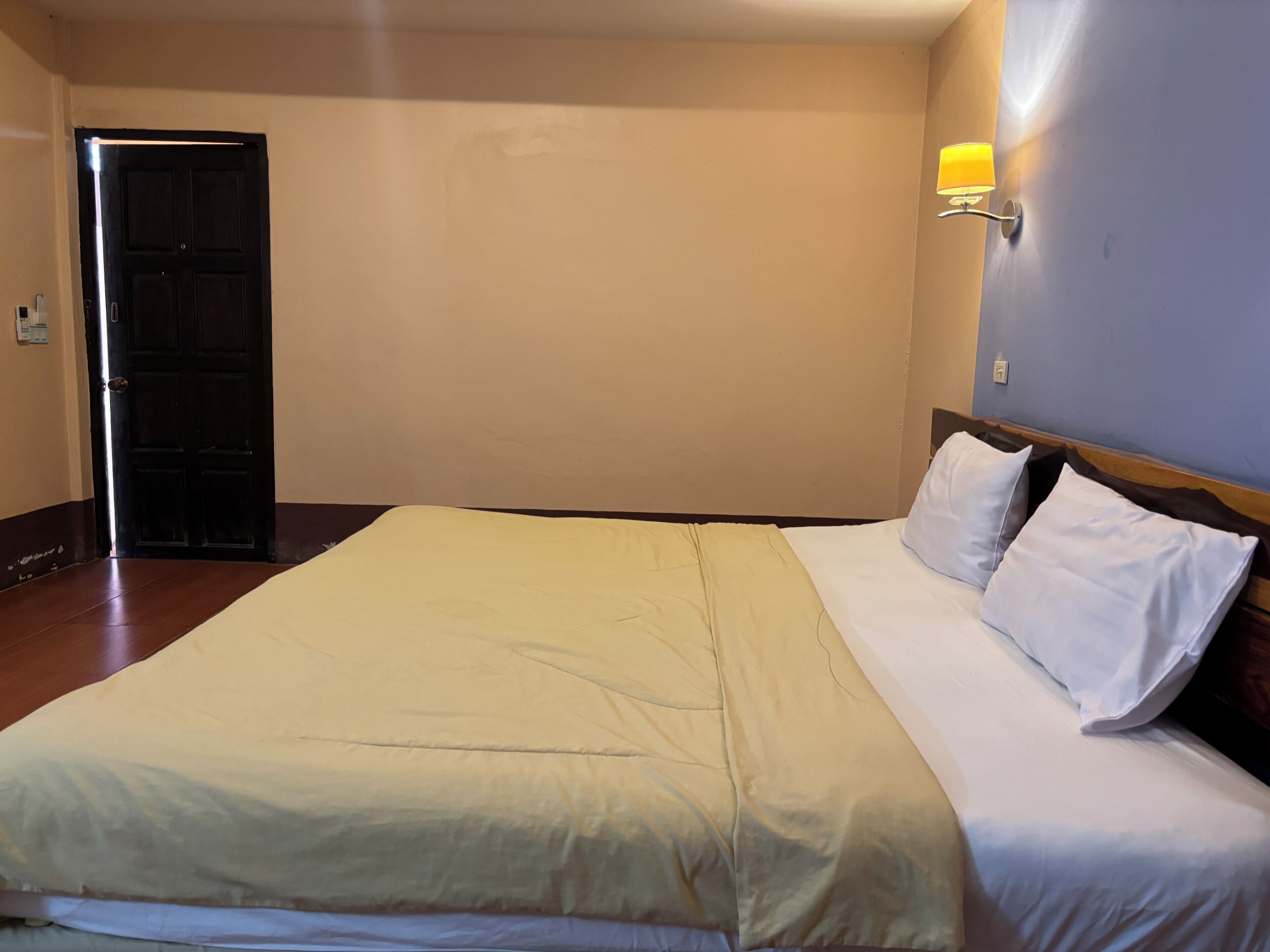 Habitación de hotel con una cama grande, una puerta y una lámpara fijada a la pared.
