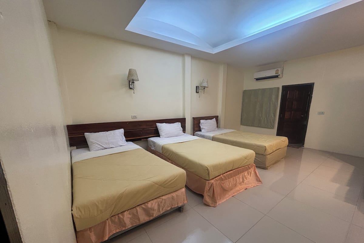 A hotel room with three beds, a skylight, a wall-mounted air conditioner, and a door.