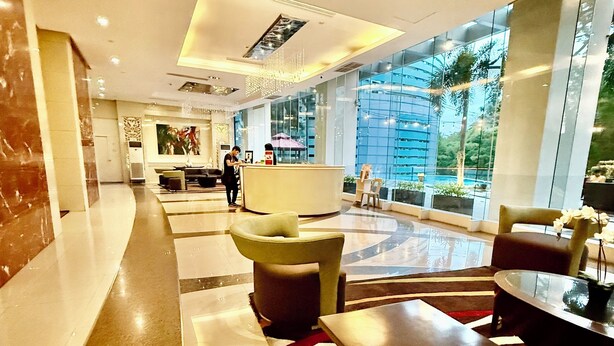 A hotel lobby with a reception desk, seating area, and large windows offering a view of the outdoors. - Executive Suites Bellagio Golf View Residences (Taguig)