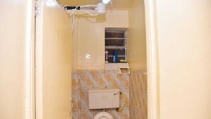 A small, enclosed bathroom with a toilet, a shelf with toiletries, and a window. - Cozy 1-bedroom bed & breakfast in Nairobi, Mirema drive.
Home Away From Home (Nairobi)