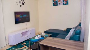 A modern living room with a flat-screen TV mounted on the wall, a white cabinet, a teal sofa, and a coffee table. - Cozy 1-bedroom bed & breakfast in Nairobi, Mirema drive.
Home Away From Home (Nairobi)
