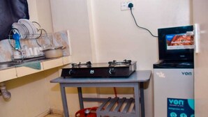 A kitchen with a gas stove, a red gas cylinder, a dish rack, and a television displaying a cooking program. - Cozy 1-bedroom bed & breakfast in Nairobi, Mirema drive.
Home Away From Home (Nairobi)