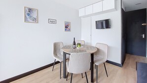 A modern dining area with a round table, four chairs, a bottle of wine, and a small decorative item. There are framed pictures on the wall and a television mounted above the table. - Apartment Brelin by Interhome (Les Menuires)