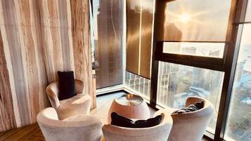 A modern living room with a large window, wooden flooring, and a city view.