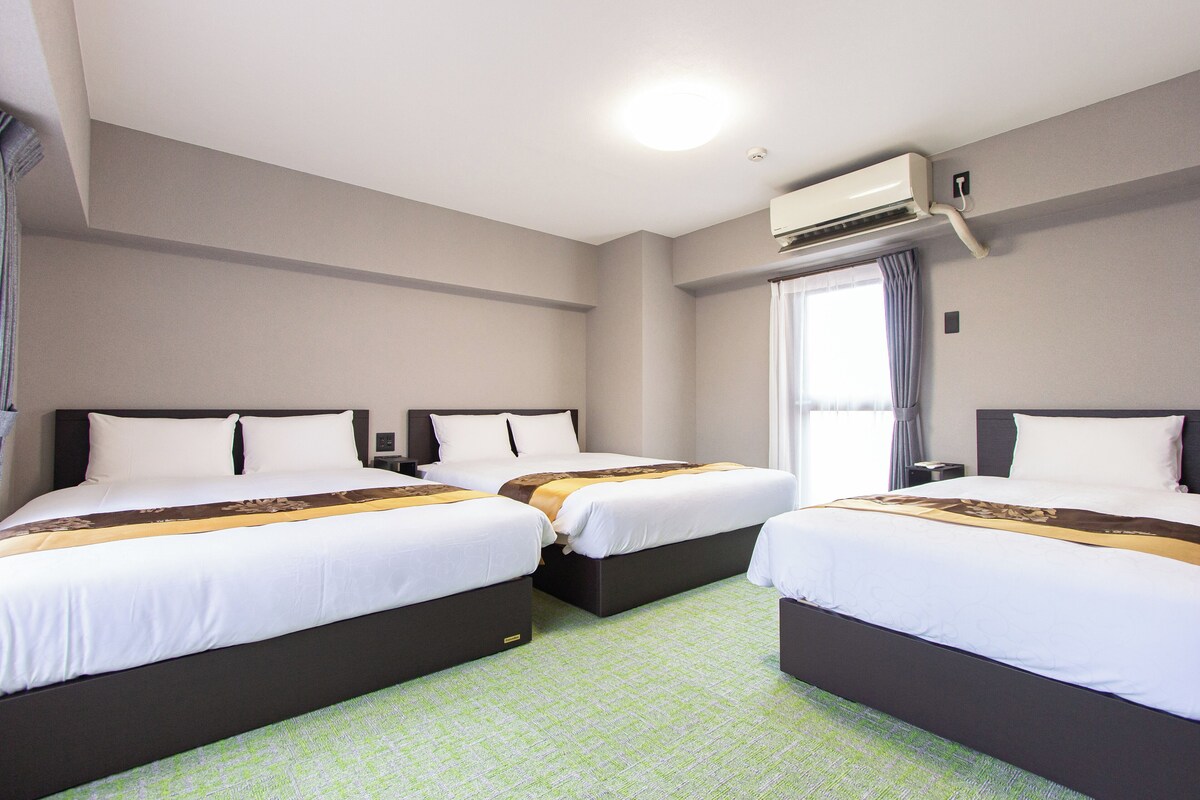 A hotel room with two beds, a window with curtains, an air conditioning unit, and a green carpet.
